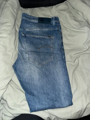 Blå jeans från G-Star RAW - Snygga blå jeans från G-Star RAW med klassisk femficksdesign och diskret logga på bakfickan. Jeansen har en rak passform och är tillverkade i mjukt denimtyg som ger en cool och avslappnad look. Perfekta för dig som gillar streetstyle.