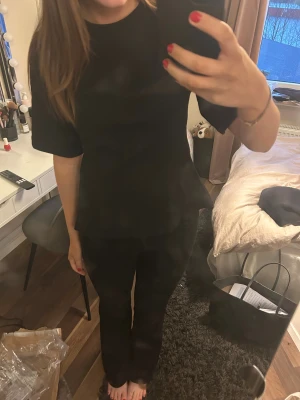 Svart topp med öppen rygg - Säljer en svart topp med korta ärmar och snygg peplumform. Baksidan har öppen rygg med två knytningar som ger en cool och trendig look. Perfekt för dig som vill sticka ut lite extra! Materialet känns mjukt och lätt. Ny med prislapp.