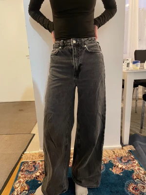 Svarta wide jeans med hög midja - Säljer ett par svarta jeans med breda ben och hög midja. Jeansen har klassisk femficksdesign, silverfärgade knappar och dragkedja. Perfekta för dig som gillar en avslappnad och trendig look.