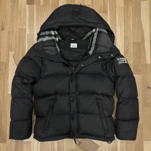 Burberry Pufferjacka Svart - Säljer denna svarta Burberry jackan då den var lite för liten på mig, jackan är en perfekt julklapp då den är varm och bekväm inför vintern, luvan är fodrad med ett varmt material som håller dig varm året runt. Den har även fleece fodrade fickor som är otroligt varma och bekväma.  Jackan är använd en gång när jag testade den men användes aldrig utomhus. Den går att göra till en väst genom att ta av ärmarna genom ärm-zippersen! Tveka inte att fråga om ni funderar över något! Storlek S!  ☃️❄️