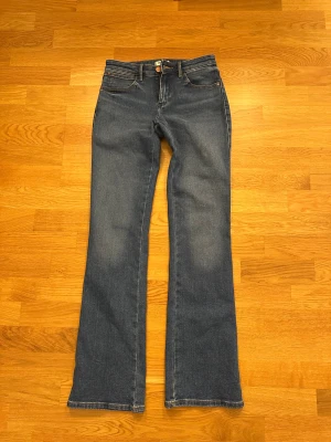 Bootcut jeans  - Snygga blå bootcut jeans från Wrangler med klassisk femficksdesign och bruna detaljer på knapp och läderpatch. Jeansen har en mörk tvätt och är tillverkade i slitstarkt denim med gul kontrastsöm. Perfekt passform med normal midja och bootcut-ben. Innerbenslängd: 80cm. Superfint skick, inga slitningar eller likande. Storlek: W25 L32