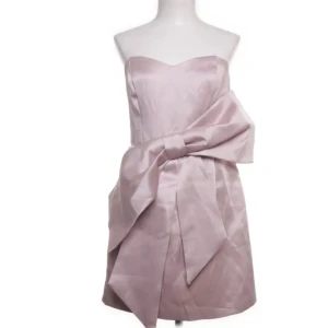 Klänning med rosett - Superfin ljusrosa axelbandslös klänning i satin med stor rosett framtill. Klänningen har en kort längd och en snygg, figurnära passform. Perfekt för dig som vill sticka ut med en elegant och trendig look.🎀