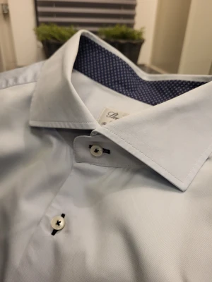 Ljusblå skjorta Stenströms, storlek 46 - Snygg ljusblå skjorta från Stenströms i fitted body-modell. Skjortan har klassisk krage, vita knappar och coolt mönstrat mörkblått tyg på insidan av kragen och manschetterna. Tillverkad i exklusiv twofold super cotton för en lyxig känsla.