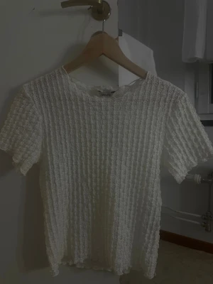 Vit spetsblus från AWARE - Säljer en söt vit blus från AWARE med korta ärmar och ett genombrutet spetsmönster. Blusen har en rak passform och är tillverkad i ett lätt och luftigt material som passar perfekt till varmare dagar. Supersnygg att styla med jeans eller kjol!