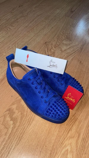 Blå Christian Louboutin sneakers mocka - Säljer ett par sjukt snygga blå sneakers från Christian Louboutin i mocka. Skorna har coola nitar på tån, matchande blå snörning och en platt sula. Kommer med originalkartong och kort. Perfekta för dig som vill sticka ut med exklusiv stil. Låda, kort och allt sånt finns med 
