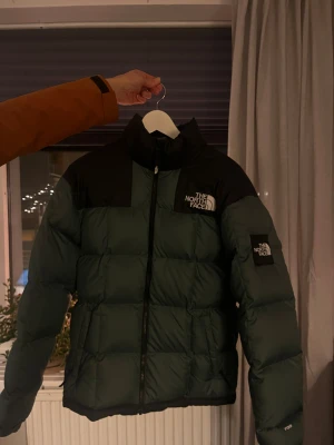  The North Face jacka - Säljer en grön och svart pufferjacka från The North Face, modell 700. Jackan har hög krage, broderad logga på bröstet och ärmen, samt dragkedja framtill. Fylld med dun och har en boxig, loose passform som är perfekt för kalla dagar.