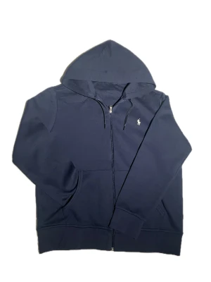 Ralph Lauren Hoodie - Säljer denna riktigt feta Ralph Lauren Zip Hoodie i Navy blue. Hoodien är äkta men saknar lappen i nacken då den är köpt från grossist. Hoodien är även sydd i nacken för att täcka upp hålen där lappen satt. Skick - 10/10. Storlek - M. Färg - Navy Blue. Skriv om du har fler frågor.