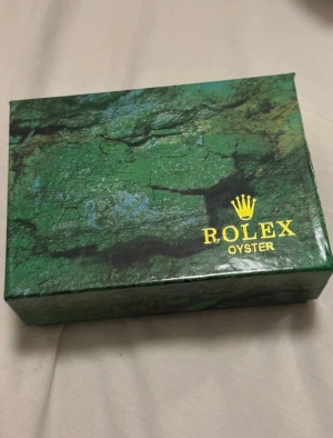 Grön klockask - Säljer en snygg grön klockask. Material papp/ kartong.  Perfekt för att förvara eller ge bort din klocka. Boxen har en lyxig känsla och klassisk design med logga på locket.