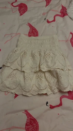 volangkjol från Zara - Supersöt krämvit kortkjol från Zara med bred resår i midjan och två lager volanger. Kjolen har broderade blommönster och vågiga kanter, super söt sommar kjol