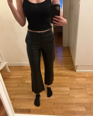 Svarta croppade byxor i skinnimitation - Svarta skinnbyxor croppad längd och raka, lite vidare ben. Fickor i fram 🤍 Jag är 168 cm lång.