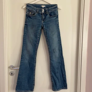 Blå bootcut jeans från Gina Tricot - Snygga blå jeans från Gina Tricot i storlek 164. Modellen har bootcut-ben, klassiska fem fickor och dubbla knappar i midjan. Jeansen har ljus tvätt med diskreta slitningar och kontrastsömmar. Perfekt för dig som gillar retrovibbar och bekväm passform. Defekter på tyget finns på benen.