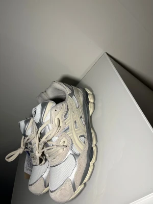 Asics GEL sneakers i beige och silver - Snygga Asics GEL sneakers i beige och silver med mesh och mockadetaljer. Skorna har rund tå, snörning och en chunky platt sula som ger en sportig vibe. Perfekta för dig som gillar retrostil och vill ha bekväma sneakers med cool design.