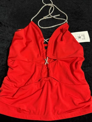 Röd glittrig korsettopp från Bik Bok - Snygg röd korsettopp från Bik Bok med glittriga silverband som halsrem och dekorativ snörning framtill. Toppen är delvis croppad med rynkade sidor som ger en fin siluett . 