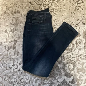 Mörkblå jeans från Lee - Snygga mörkblå jeans från Lee med klassisk femficksdesign och diskret slitning på benen. Jeansen har rak passform och normal midja, vilket ger en clean och tidlös look. Perfekta för dig som gillar stilrena och bekväma jeans.