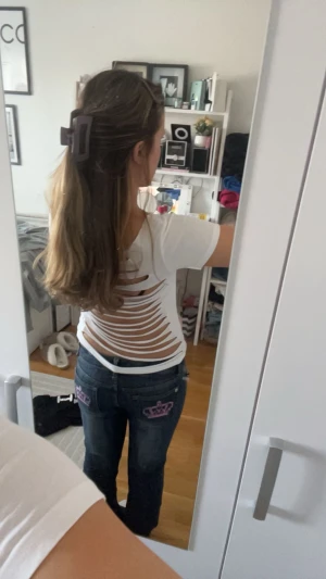 Vit topp med slitsad rygg - Säljer en vit kortärmad topp med coola slitsdetaljer över hela ryggen. T-shirten har en rund halsringning och är figurnära i modellen. Perfekt för dig som vill sticka ut med en edgy och trendig look.