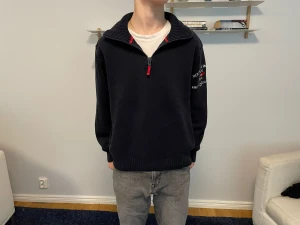 Quarter zip från Henry Lloyd - Mörkblå Quarter zip från Henry Lloyd. Tröjan är i bra skick förutom ett litet hål i armhålan, vilket knappt är märkbart. Riktigt stiligt tillsammans med ett par gråa jeans. Modellen är 173cm och tröjan är storlek S.