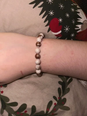 Brunt och vitt pärlarmband - Snyggt armband med pärlor i brunt och vitt, trädd på elastisk tråd. Pärlorna är runda och har en glansig finish som ger en stilren och enkel look. Perfekt för dig som gillar minimalistiska accessoarer med en touch av retro.