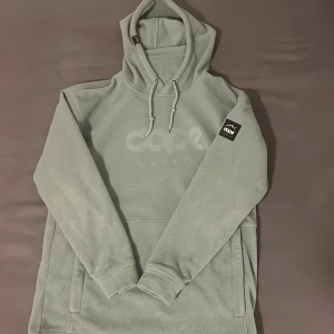 Ljusgrön fleece hoodie från Dope - Säljer en ljusgrå hoodie från Dope med broderad logga på bröstet och patch på ärmen. Tröjan är i mjuk fleece, har huva med snörning och en stor magficka. Perfekt för kalla dagar och chill stunder. Passformen är normal och ärmarna är långa.