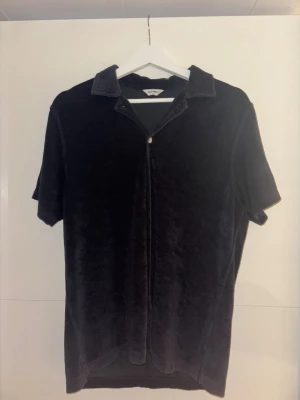 Mörkblå frottéskjorta från East West - Svart skjorta i mjuk frotté från East West. Skjortan har korta ärmar, klassisk krage och knäppning framtill med ljusa knappar. Perfekt för sommarn och avslappnad stil, med en loose fit som ger skön känsla. Använd fåtal gånger vilket för den väldigt bra skick nästan som ny.