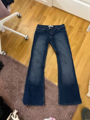 Blå bootcut jeans från Hilfiger - Snygga blå jeans från Hilfiger med bootcut passform och klassisk femficksdesign. Jeansen har en mörk tvätt med lätt slitning framtill och bakfickor med lock. Materialet är jeans och midjan är normal. Perfekta för dig som gillar retrovibbar och bredare ben.