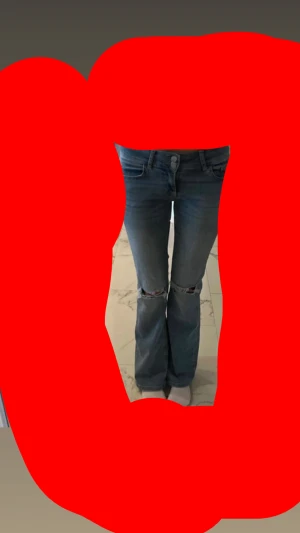 Blå bootcut jeans med slitna knän - Säljer ett par blå jeans med bootcut passform och snygga slitningar vid knäna. Jeansen har klassisk femficksdesign, knapp och dragkedja framtill samt låg midja. Perfekta för dig som gillar en chill och trendig stil.