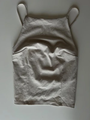 Beige linnetopp med snörning - Säljer en stilren beige linnetopp med raka linjer och smala axelband. Toppen har snörningsdetaljer på baksidan som ger en snygg och justerbar passform. Materialet känns mjukt och lätt, perfekt för varma dagar. Enkel och clean design som är lätt att matcha.