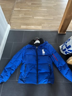Blå pufferjacka från Polo Ralph Lauren - Säljer en blå pufferjacka från Polo Ralph Lauren med stor vit logga på bröstet. Fint skick och har kvar att ge, finns mer bilder i pm. 