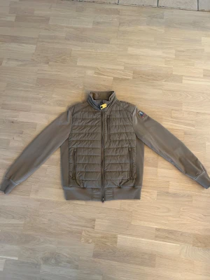 Beige pufferjacka från Parajumpers S - Snygg beige pufferjacka från Parajumpers med quiltad front och rygg, samt släta ärmar. Jackan har dragkedja framtill, ståkrage och två fickor med dragkedja. Patch med logga på ena ärmen. Använts sparsamt under 1-2 månader så i nästintill perfekt skick. Nypris 4200
