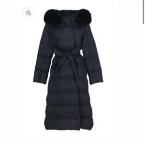 Lilly jacket Stockholm fur  - Snygg lång svart dunjacka med stor fluffig pälskrage och bälte i midjan. Jackan har quiltad design och långa ärmar, perfekt för kalla dagar. Ger en riktigt cool och lyxig vibe till vinterlooken. Köpte den i år i mars för 2799kr storlek m/l