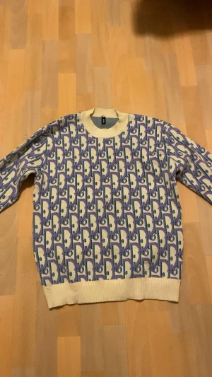 Dlor sweatshirt - Unik stickad tröja från Dlor med ett grafiskt mönster i lila, grönt och vitt. Tröjan har rund hals, ribbade muddar och nederkant. Perfekt för dig som gillar färg och vill sticka ut lite extra.