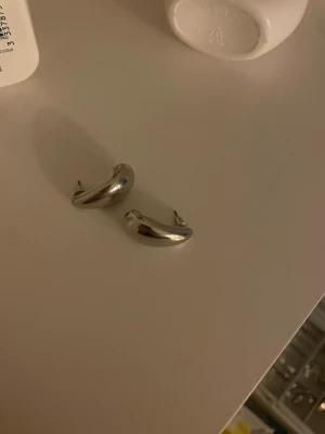 Chunky silverfärgade örhängen - Säljer ett par chunky örhängen i silverfärg med mjukt böjd, organisk form. De har stift och är perfekta för dig som gillar minimalistisk men ändå statement stil. Passar till alla tillfällen och ger en cool touch till din look.