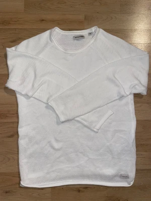 Vit stickad tröja från Jack & Jones - Säljer en vit stickad tröja från Jack & Jones med rund hals och långärmad design. Tröjan har en enkel och clean look med diskret logga vid nederkanten. Perfekt för dig som gillar stilrena och bekväma plagg.