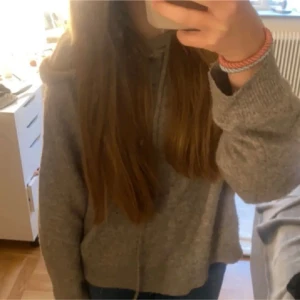 Beige stickad hoodie med huva - Mysig beige stickad hoodie från Lindex med huva och snörning. Tröjan har långärmade ärmar och ribbade muddar vid ärmslut och nederkant. Perfekt för dig som gillar chill och enkel stil. Passar dig som vill ha en loose fit.