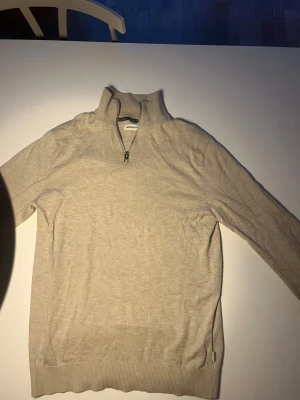 Beige half zip tröja Jack & Jones - Snygg beige långärmad tröja från Jack & Jones med half zip och hög krage. Tröjan är tillverkad i mjuk bomull och har en clean look med ribbade muddar vid ärmslut och nederkant. Perfekt för dig som gillar stilrena och enkla plagg.