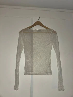 Vit långärmad spetsblus från Kappahl  - Säljer en tunn och transparent vit blus från Kappahl med lång ärm och rund hals. Blusen är gjord i ett mjukt spetsmaterial med diskret mönster och har en slim passform som sitter snyggt på kroppen. Perfekt för att styla lager på lager eller med ett linne under.