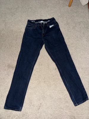 Mörkblå jeans från Vailent - Snygga mörkblå jeans från Vailent med klassisk femficksdesign och brunt läderpatch bak i midjan. Jeansen har raka ben och kontrastsömmar, vilket ger en stilren look. Perfekta för dig som gillar enkel och tidlös denim. Med måtten W29 L32