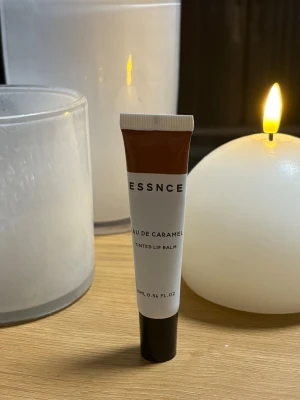 ESSNCE Eau de Caramel Tinted Lip Balm - Tintat läppbalsam från ESSNCE i färgen Eau de Caramel. Kommer i en smidig tub på 10 ml med vit och brun design samt svart kork. Ger en mjuk karamellton till läpparna och återfuktar samtidigt. Perfekt att ha i väskan för en fräsch look. Oanvänd öppnad sedan idag 25/11