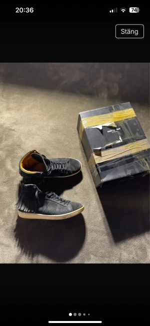 Saint Laurent svarta mocka sneakers - Svarta high-top sneakers från Saint Laurent i mocka med fransdetaljer längs skaftet och snörning framtill. Insidan är fodrad i lyxigt gult skinn och yttersulan är vit med Saint Laurent Paris-logga undertill. Snygg och unik design som sticker ut.