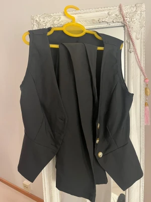 Svart kostymset - Stilren svart väst med v-ringning och tre pärlemorskimrande knappar framtill. Västen har figursydd passform och lätt utsvängd nederkant som ger en snygg siluett. Med svarta kostymbyxor