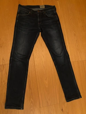 Mörkblå slim jeans från Wrangler - Snygga mörkblå jeans från Wrangler med klassisk femficksdesign och diskreta slitningar. Modellen är slim med smal passform och har dragkedja i gylfen. Jeansen är tillverkade i stretchigt denim för extra komfort och har Wrangler-logga på bakfickan.