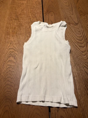 Vit ribbad linnetopp från Gina Tricot - Säljer en vit ribbad linnetopp i storlek S från Gina Tricot, basically basics-kollektionen. Toppen är ärmlös med rund hals och har en fin passform. Perfekt att styla med jeans eller kjol för en clean och fräsch look.