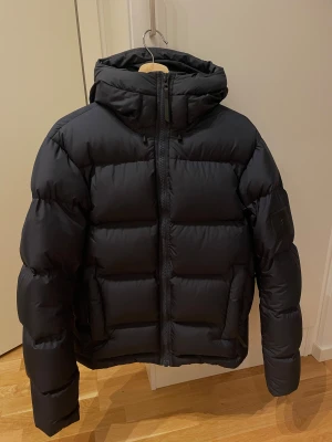 Peak Performance dunjacka M - Säljer en mörkblå dunjacka från Peak Performance i storlek M. Jackan har huva, dragkedja framtill och diskret logga på ärmen. Den är rejält vadderad och har en clean, boxig siluett som är perfekt när det är kallt. Nypris: 3999 kr, använd fåtal gånger. 