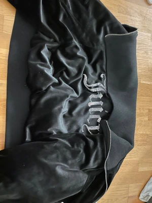 Svart velour bomberjacka Juicy Couture XL - Svart bomberjacka från Juicy Couture med en stor glitter logga på ryggen,Perfekt för dig som vill ha en ikonisk och comfy look. Den är i storlek XL men passar på mej som är xs-s jag tycker bara jag får breda axlar i den därför väljer jag att sälja den, den är aldrig använd och i topp skick, jag är inte säker men jag tror inte den här säljs längre så passa på, den passar nog alla storlekar beroende på hur man vill att den ska sitta, hör av er vid intresse priset kan diskuteras.