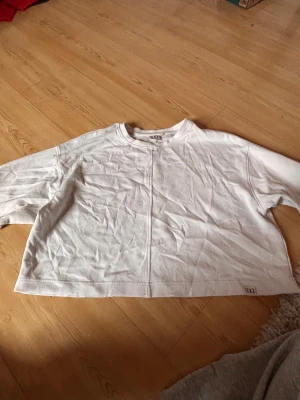 Vit croppad sweatshirt Le Don De Vie - Säljer en vit croppad sweatshirt från Le Don De Vie i storlek XS. Tröjan har lång ärm, rund hals och en synlig söm som går vertikalt både fram och bak. Materialet är mjuk bomull och passformen är loose för en chill vibe.