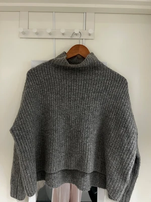 Grå ribbad polotröja  - En M men känns som en s tycker jag. Mysig grå polotröja med ribbad struktur och hög krage. Tröjan är stickad och en loose passform. Perfekt för kalla dagar när du vill vara både bekväm och snygg. 
