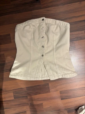 Beige tubtopp - Säljer en beige topp från HM med snygga knappar framtill och lätt utsvängd form. Vid frågor tveka inte att fråga, vid snabb affär kan priset diskuteras💞