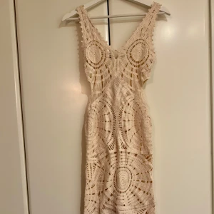 Virkad strandklänning - Superfin beige virkad långklänning med unikt cirkelmönster och breda axelband. Klänningen har en v-ringad hals och är ärmlös, perfekt för stranden.