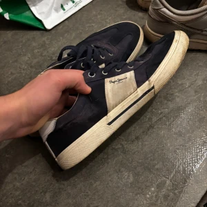 Blå sneakers från Pepe Jeans - Snygga sneakers från Pepe Jeans i mörkblått med vita detaljer och vit sula. Skorna har snörning och en klassisk låg profil. Pepe Jeans-loggan syns på sidan. Perfekta för dig som gillar stilrena och sportiga skor.