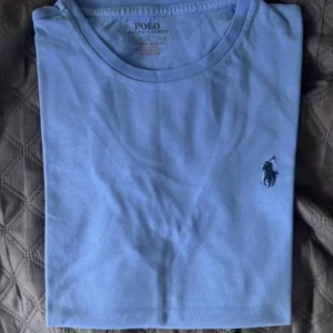 Ljusblå t-shirt från Polo Ralph Lauren - Snygg ljusblå t-shirt från Polo Ralph Lauren i bomull med klassisk rund hals och broderad mörkblå logga på bröstet. Perfekt för dig som gillar stilrena och enkla plagg. Äkta vara köpt från Zalando, knappt använd pga storleken. Storlek S. 