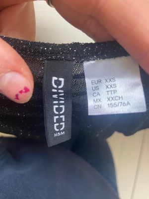 Svart glittrig mesh-top från H&M Divided - Säljer en svart långärmad mesh-top från H&M Divided i storlek XXS. Toppen har glittriga detaljer och är figurnära med rynkade sömmar längs hela plagget. Perfekt för dig som gillar en trendig och snygg look med lite extra glitter. Parfekt till nyår eller jul. 